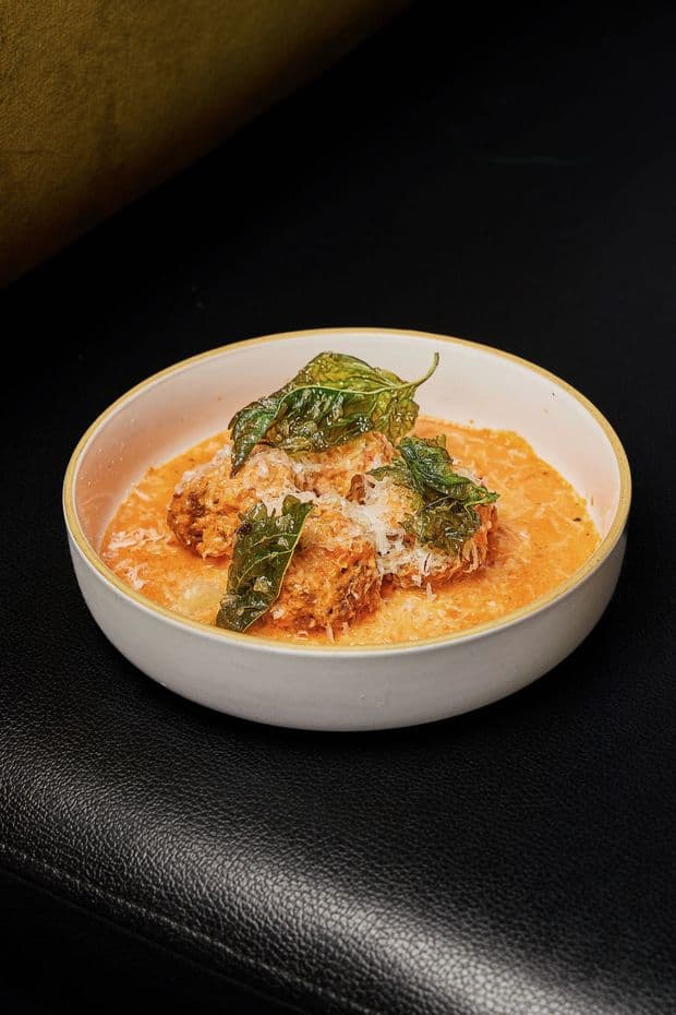 Salvatore's meatballs in tomato cream with crispy basil and grated cheese, served in a white bowl